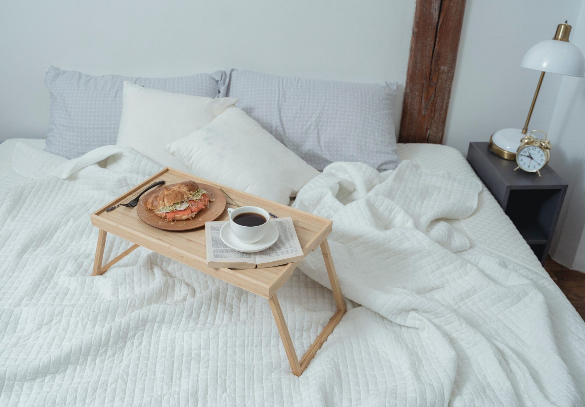 Calm bedroom with white quilted bedding, a wooden breakfast tray and a brass bedside lamp