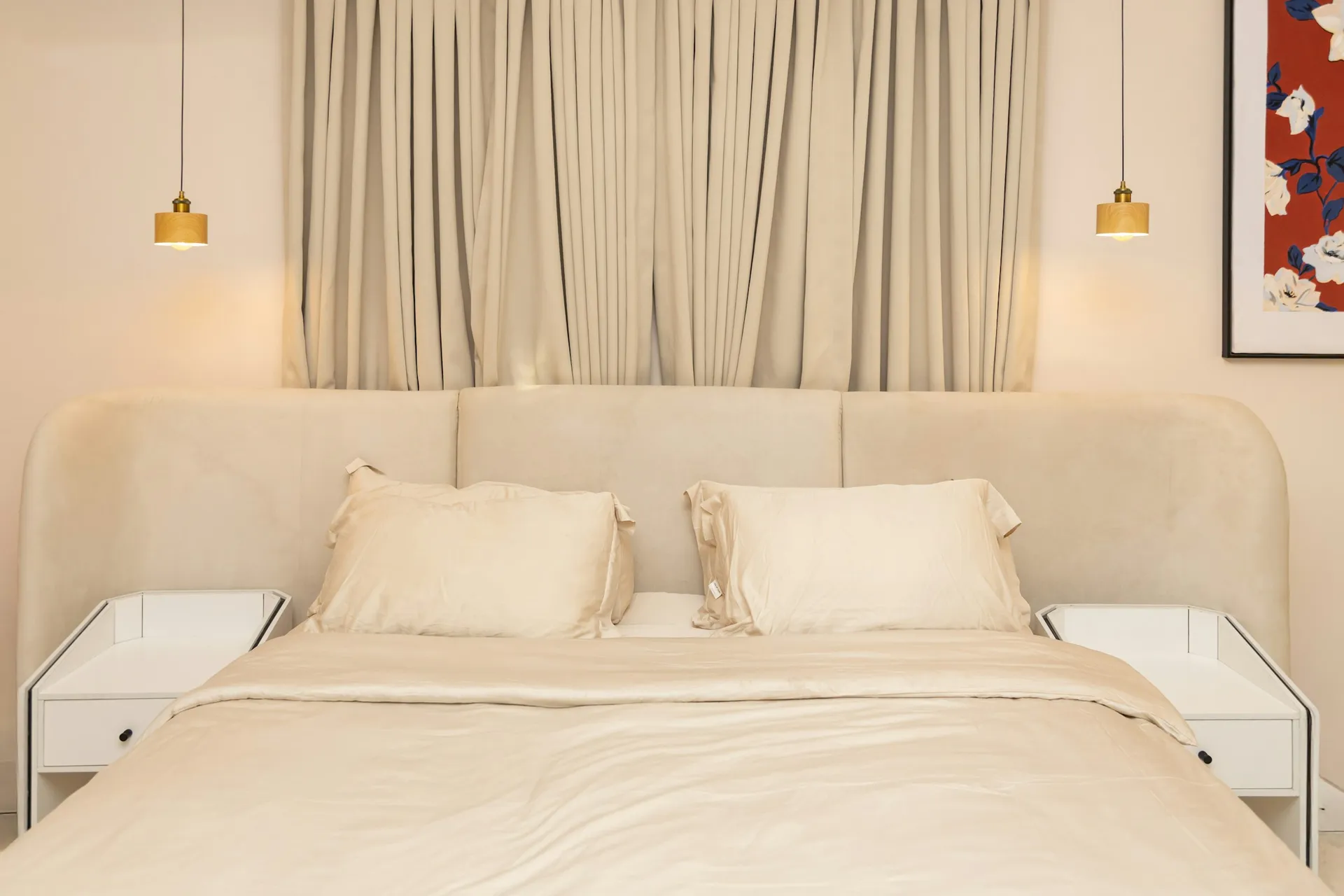 Beige upholstered bed with small pendant lights hanging over each bedside table