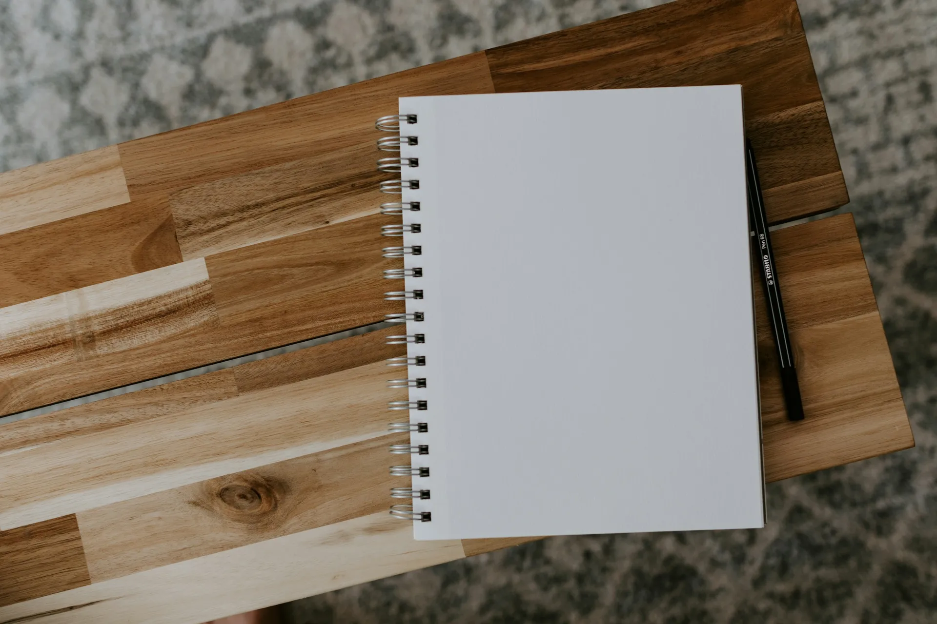 A blank spiral notebook and a pen on a wooden table