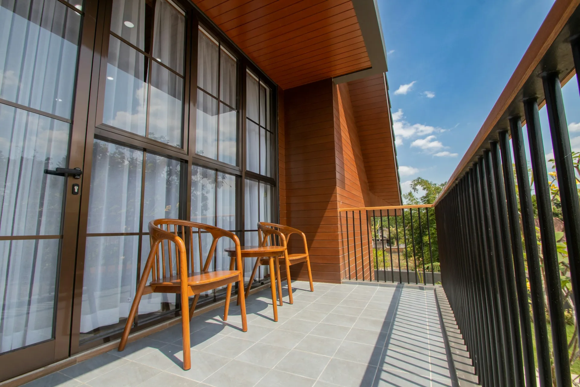 Long narrow balcony with full-height glass doors, two slim wooden chairs and a timber ceiling