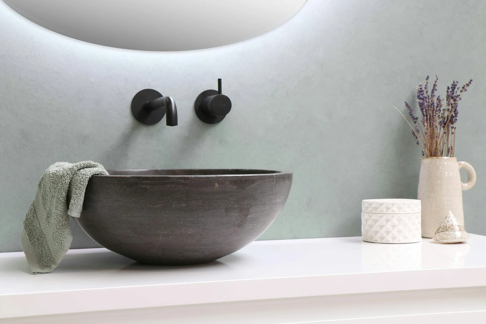 Dark stone vessel basin with black wall-mounted taps under a softly backlit wall