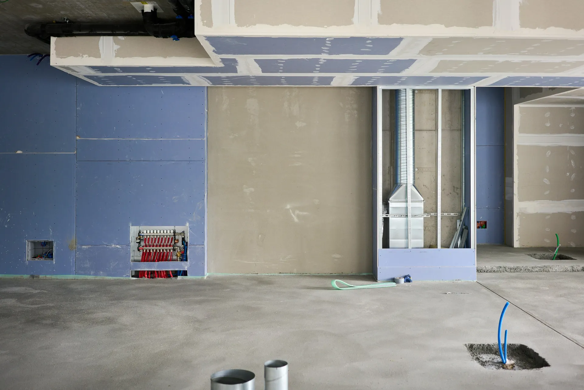 An unfinished room with an open false ceiling, bare boarded walls and paint marks on the floor