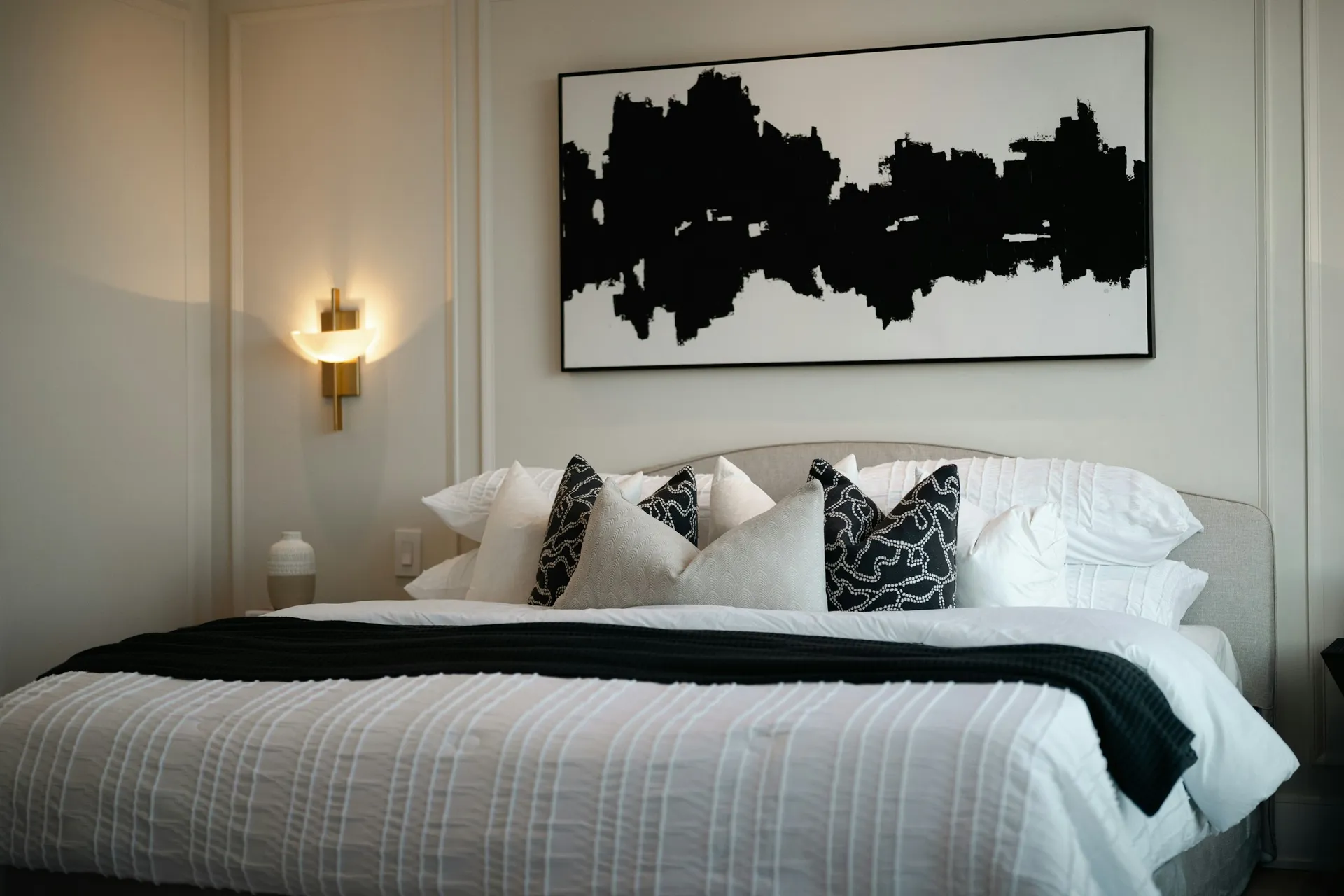 Guest bed with brass wall sconces on either side and abstract art above