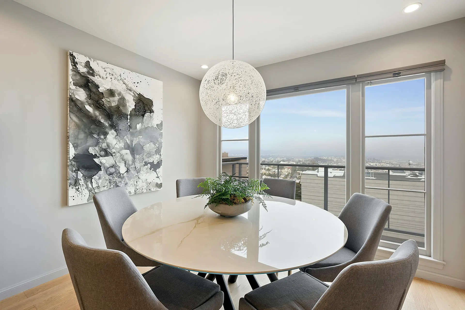 Bright dining area with a round white table, grey chairs and a globe pendant light
