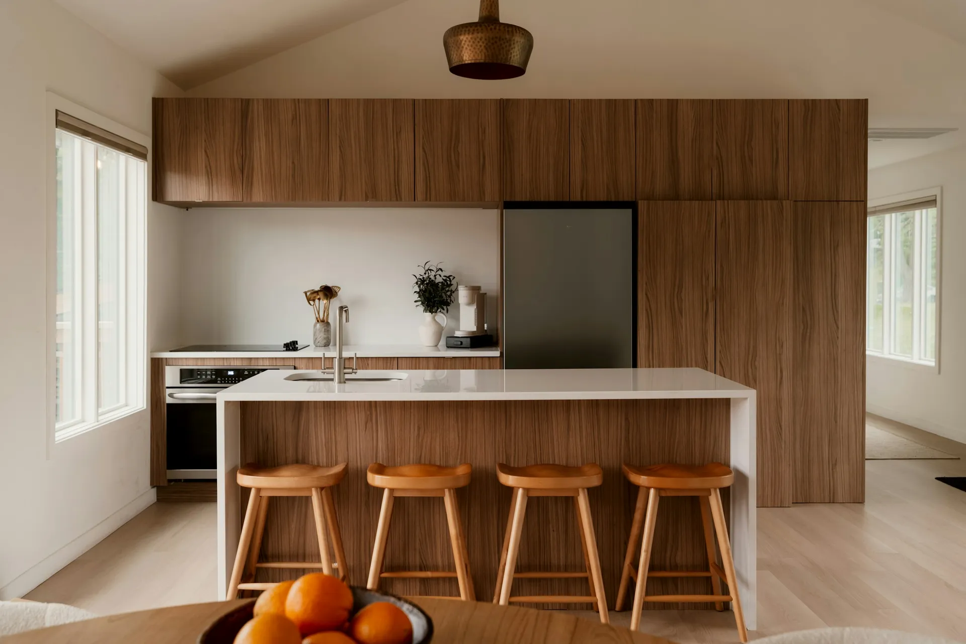 Full-height walnut kitchen cabinets behind a white island with four wooden stools