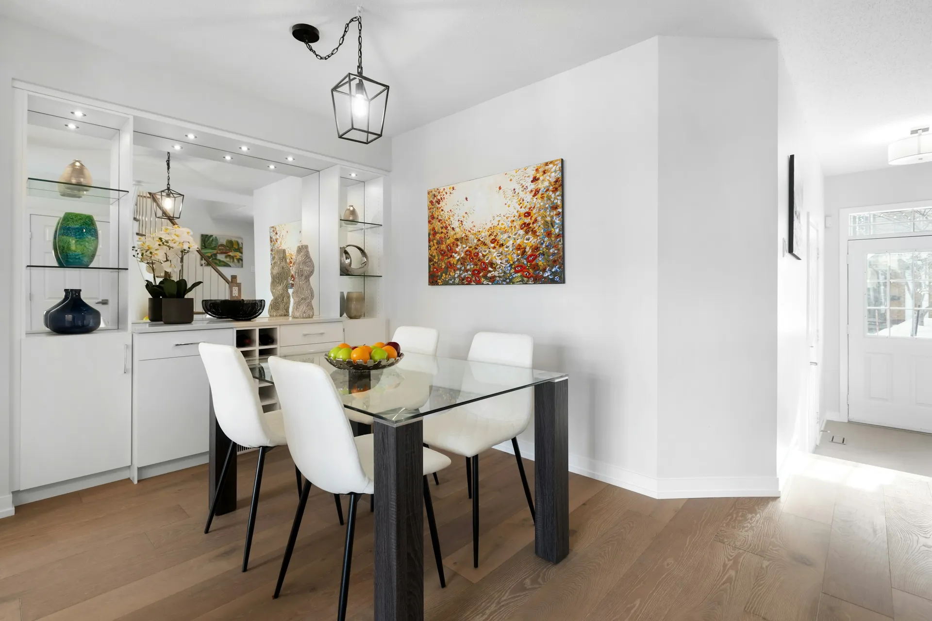 Glass dining table with white chairs next to built-in display shelves