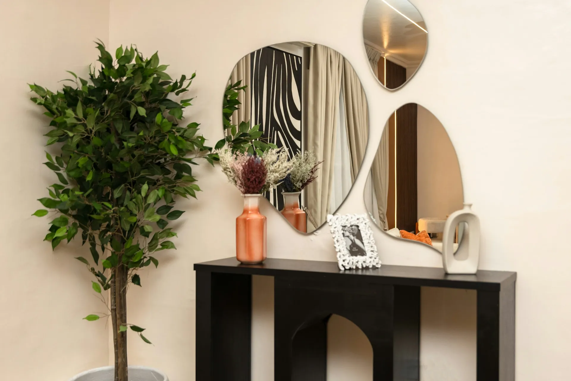 Black console table under abstract-shaped wall mirrors with a potted plant