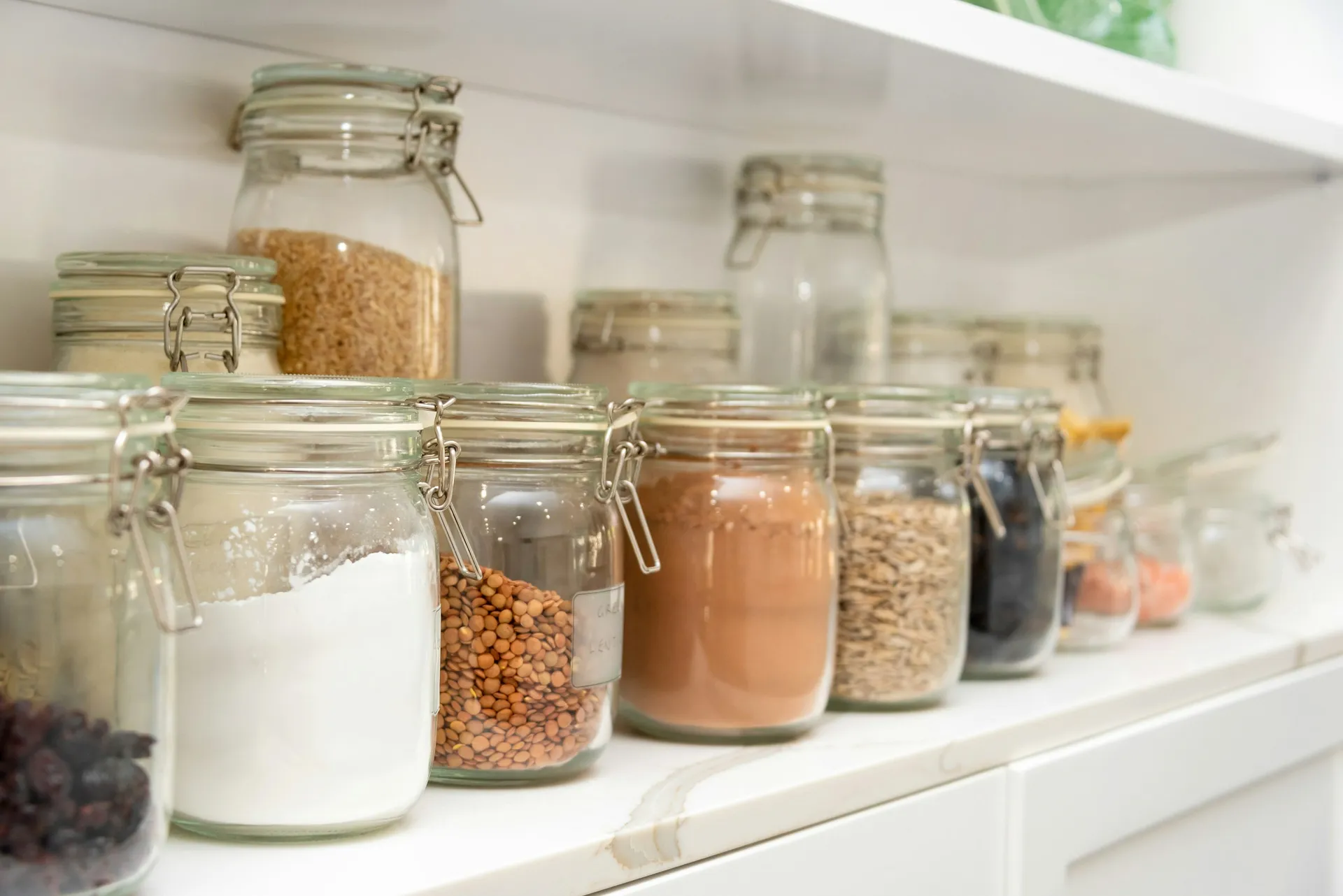 Clear glass storage jars lined up neatly on white shelves