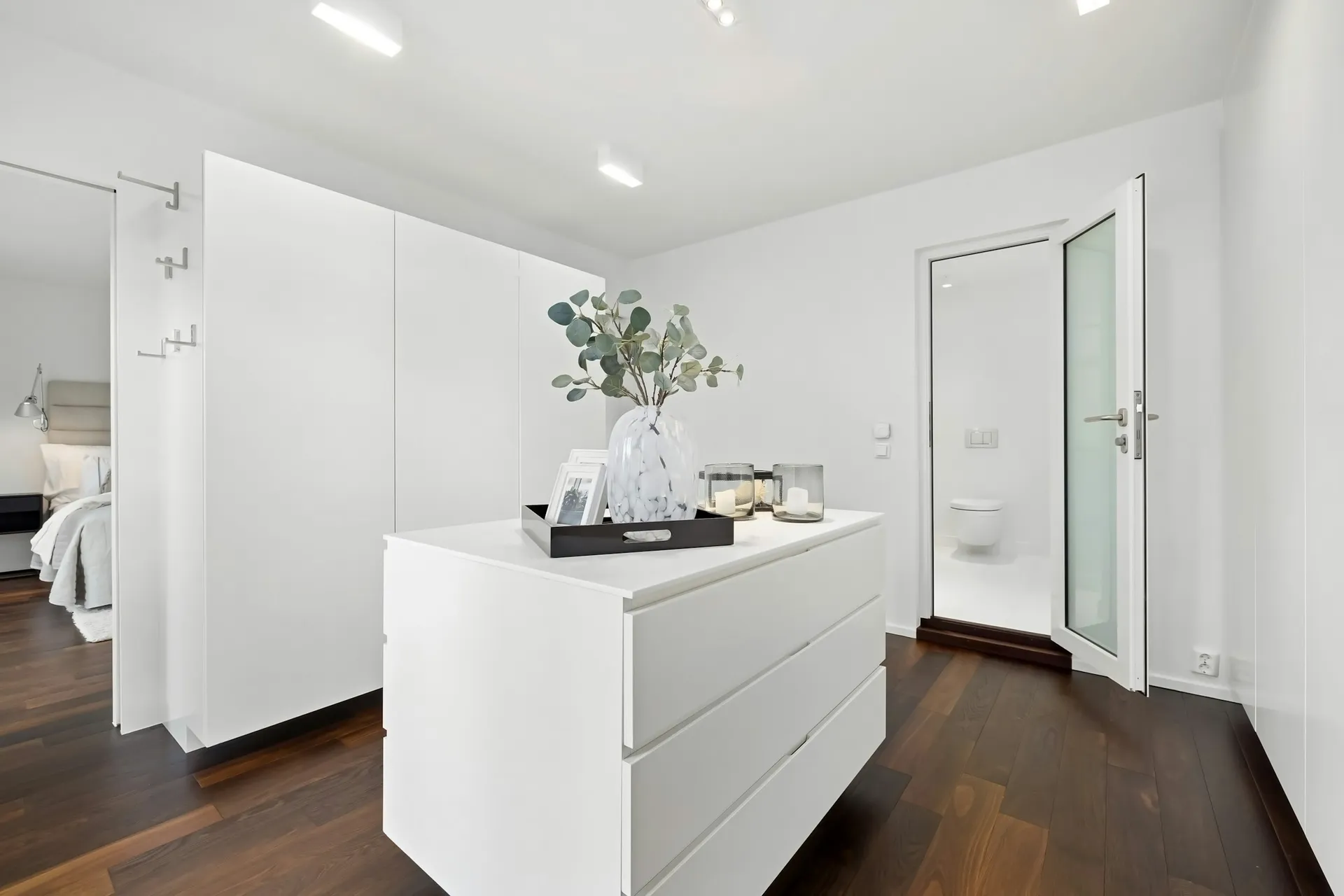 Bright dressing room with white built-in wardrobes and an island chest of drawers