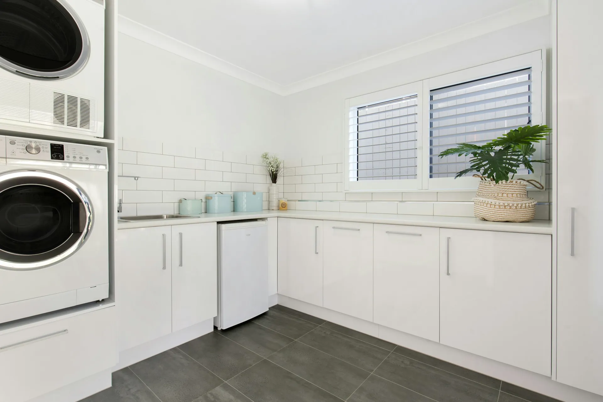 Stacked washer and dryer beside a white L-shaped laundry counter and cabinets