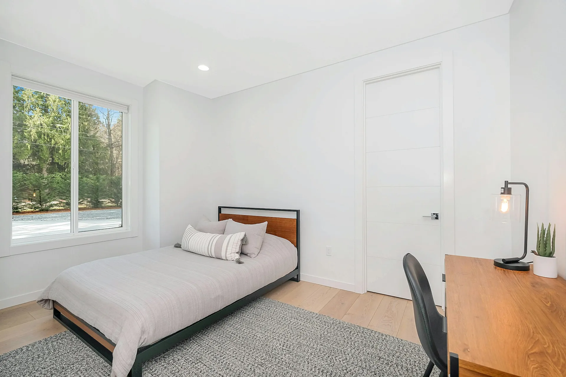 Simple bedroom with a wooden work desk and lamp beside the bed