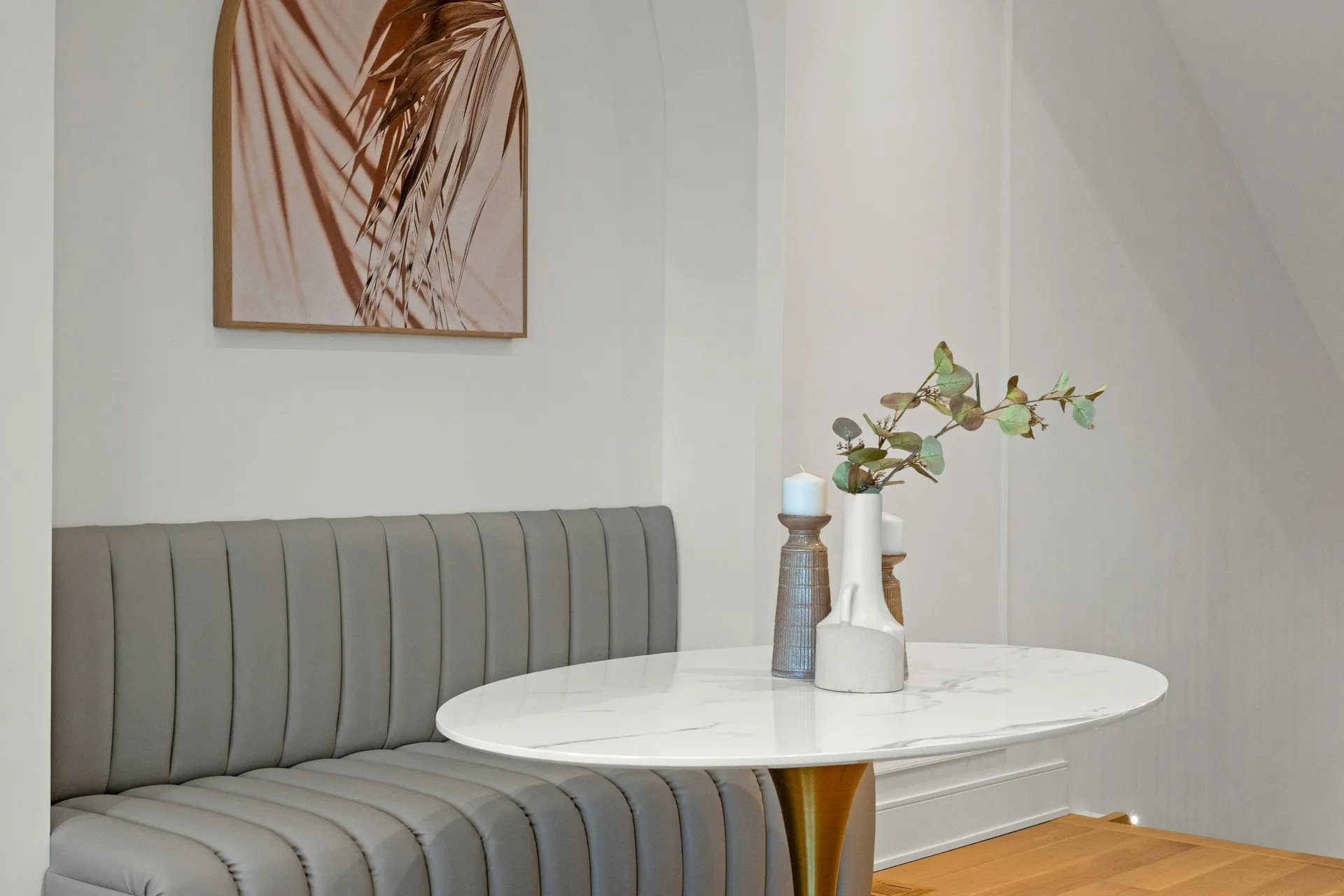 Grey upholstered banquette bench beside a round marble-top dining table