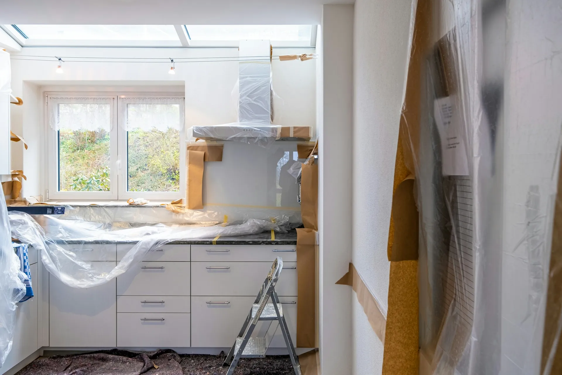 Kitchen under renovation with white cabinets covered in protective plastic and paper